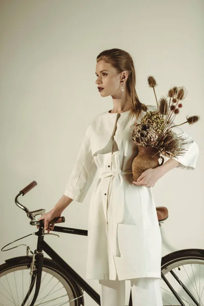 Attraente ragazza elegante in posa con mazzo di fiori secchi vicino bicicletta — Foto stock
