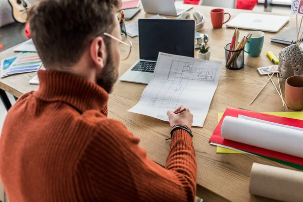 Back view of male architect sitting at computer desk and working on blueprints in loft office — Stock Photo