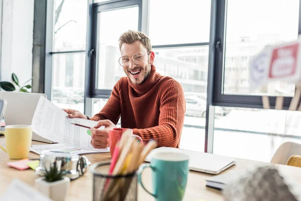 Sorridente empresário casual em óculos sentado na mesa e trabalhando no documento no escritório loft — Fotografia de Stock