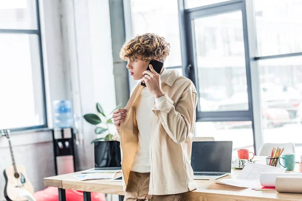 Bello architetto parlando su smartphone vicino al tavolo con cianografie in loft ufficio — Foto stock