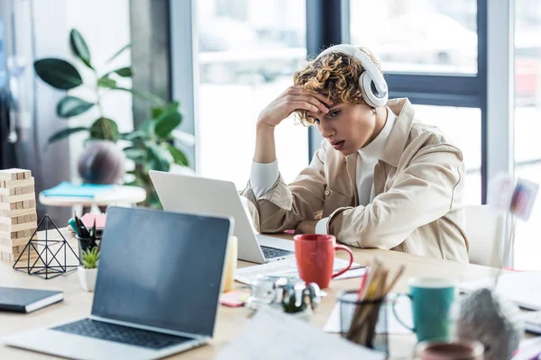 Handsome it specialist in headphones sitting at desk and using laptop in loft office — Stock Photo