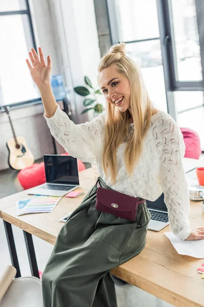 Bela mulher de negócios casual sentado na mesa de computador e acenando no escritório loft — Fotografia de Stock