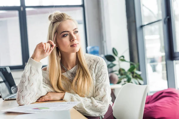 Schöne Gelegenheitsunternehmerin sitzt mit Dokument am Schreibtisch im Loftbüro und schaut weg — Stockfoto