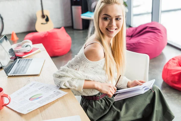 Schöne Gelegenheitsunternehmerin sitzt am Computer-Schreibtisch mit Notizbuch im Loft-Büro — Stockfoto