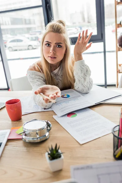 Confused casual female businesswoman sitting at table and working on graphs in loft office — Stock Photo