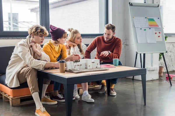 Group of female and male architects sitting at table and working on house model in loft office — Stock Photo
