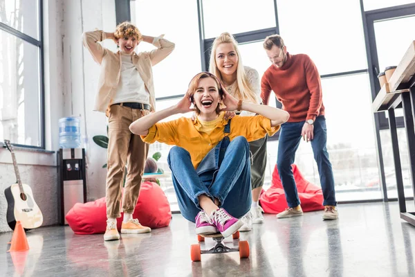 Щасливі випадкові бізнес-колеги розважаються і катаються скейтборд в офісі лофт — стокове фото