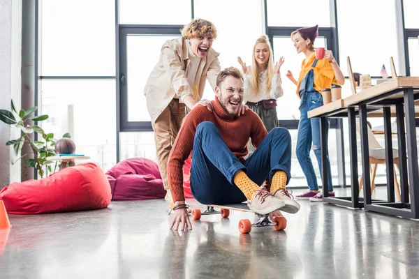 Smiling casual business colleagues having fun and riding skateboard in loft office — Stock Photo