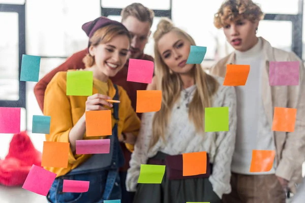 Female and male casual businesspeople looking at colorful sticky notes on glass window in office — Stock Photo