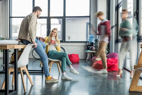 Female and male casual businesspeople sitting and having discussion in loft office with colleagues in motion blur on background — Stock Photo