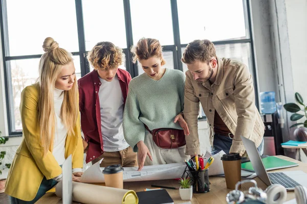 Concentrated group of female and male architects working on blueprint at desk in loft office — Stock Photo