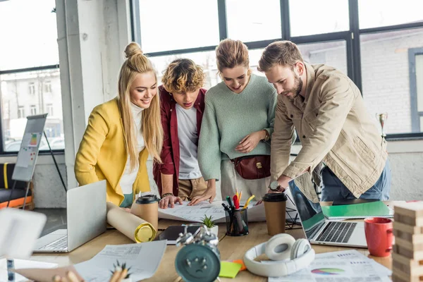 Group of female and male architects working on blueprint at desk with laptops in loft office — Stock Photo