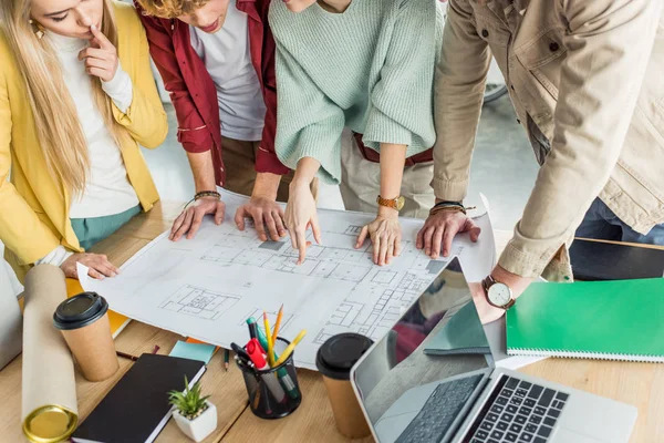 Cropped view of group of female and male architects working on blueprint at desk in loft office — Stock Photo