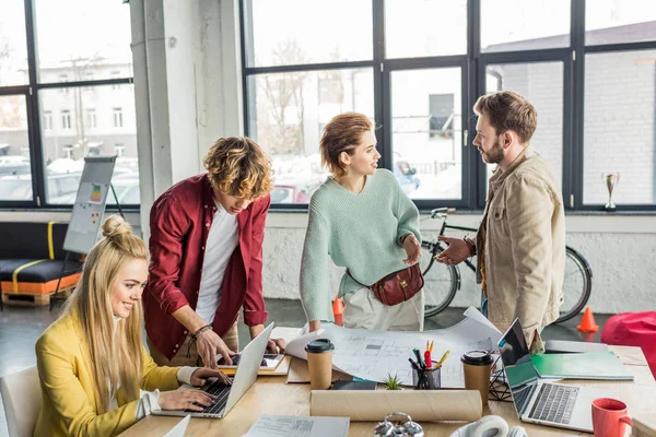 Group of female and male architects working on blueprint at desk with laptops in loft office — Stock Photo