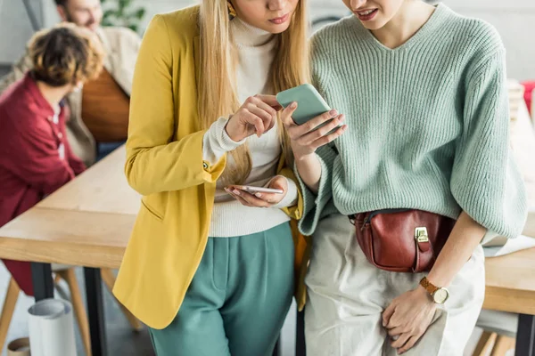 Casual businesswomen using smartphones in loft office with colleagues on background — Stock Photo