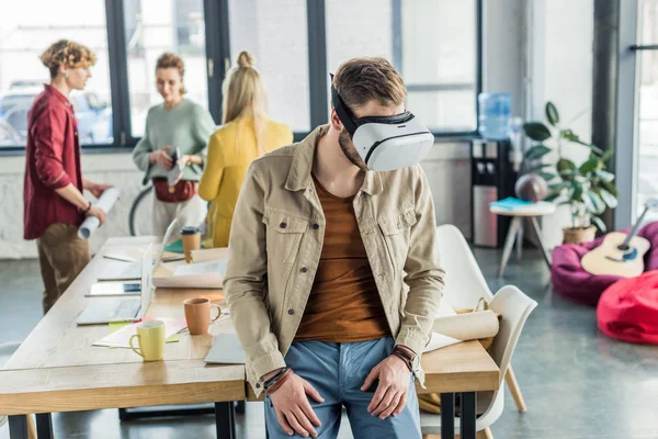 Male designer in vr headset having virtual reality experience in loft office with colleagues on background — Stock Photo