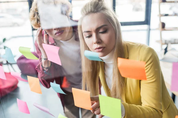 Casual businessman and businesswoman putting colorful sticky notes on glass window in office — Stock Photo