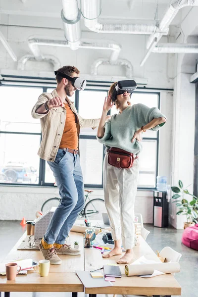 Arquitetos femininos e masculinos vestindo fones de ouvido vr, gesticulando com as mãos e tendo experiência de realidade virtual no escritório loft — Fotografia de Stock