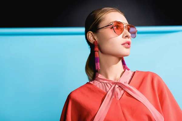 Femme à la mode posant dans des vêtements de corail vivant et des lunettes de soleil sur bleu — Photo de stock