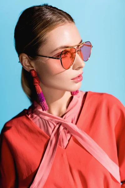 Привлекательная стильная женщина в модной живой коралловой одежде и солнечных очках, позирующих изолированно на голубом — стоковое фото