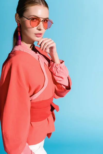 Attraente donna in abito di corallo vivente alla moda e occhiali da sole posa isolata su blu — Foto stock