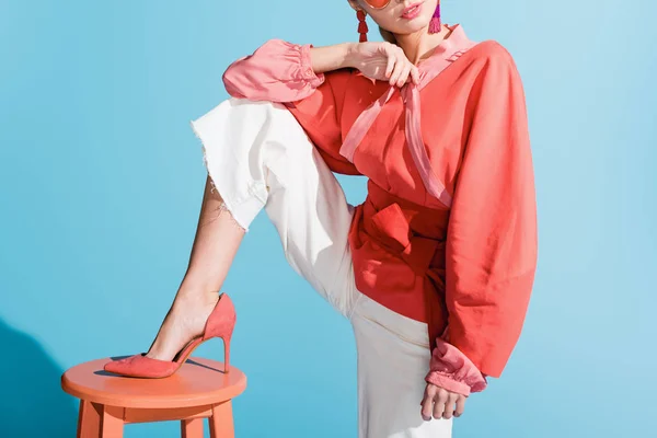 Cropped view of girl in living coral clothing posing on stool on blue — Stock Photo