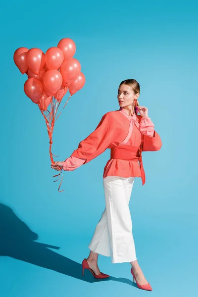 Giovane donna alla moda in posa con palloncini di corallo viventi su blu — Foto stock