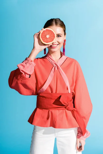 Attraktive lächelnde Frau in lebender Korallenkleidung posiert mit Grapefruit isoliert auf blauem Grund — Stockfoto