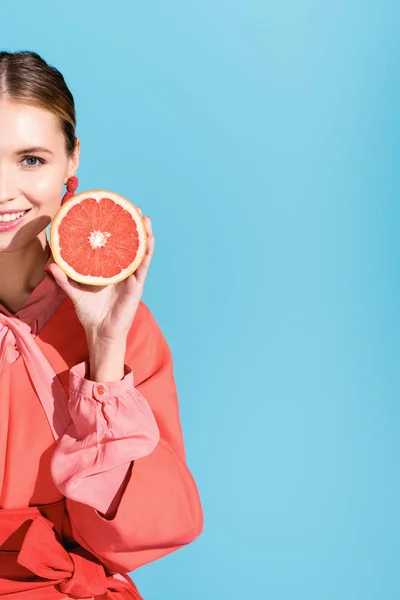 Media vista de alegre hermosa mujer posando con pomelo coral vivo aislado en azul - foto de stock