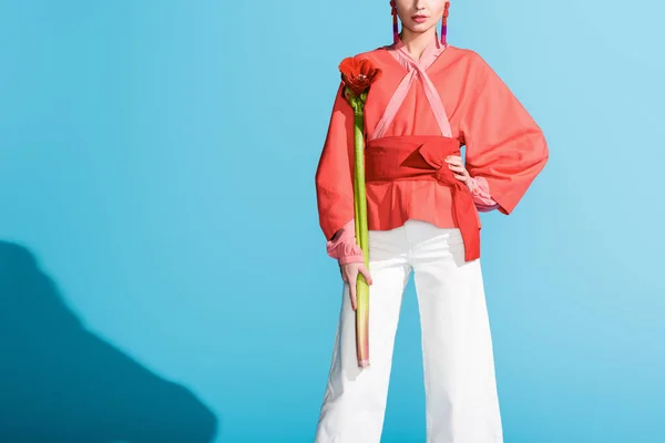 Cropped view of elegant girl holding living coral flower on blue. Pantone color of the year 2019 concept — Stock Photo