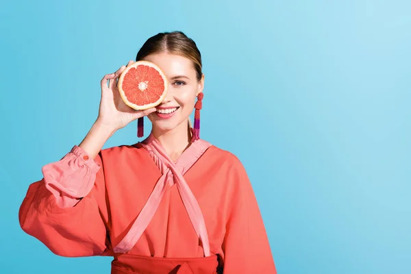 Attractive happy model in living coral posing with grapefruit isolated on blue — Stock Photo