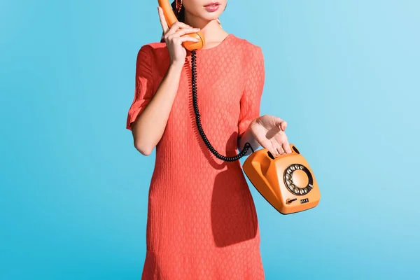 Vista recortada de la mujer en vestido de coral vivo posando con teléfono giratorio aislado en azul - foto de stock