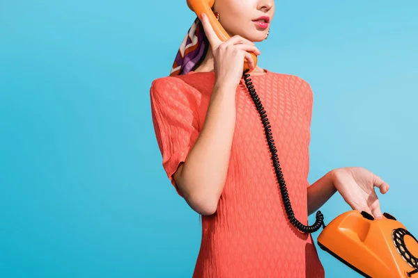 Vista recortada de chica en vestido de coral vivo posando con teléfono giratorio aislado en azul - foto de stock