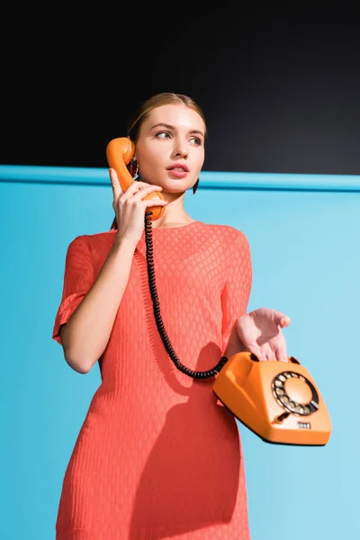 Modelo elegante em vestido de coral vivo posando com telefone rotativo em azul — Fotografia de Stock