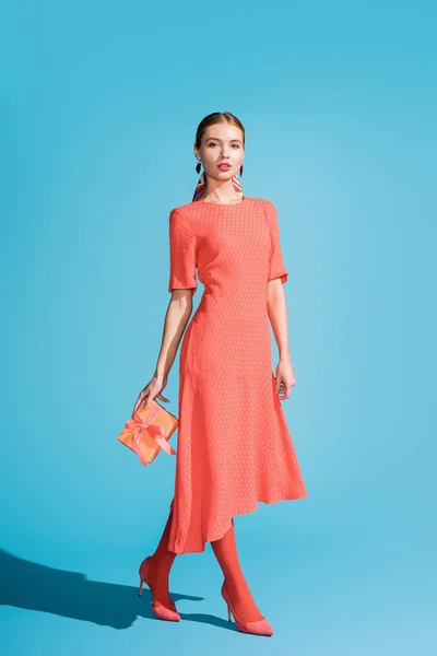 Stylish woman in living coral dress holding gift box on blue — Stock Photo