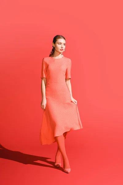 Stylish girl posing in living coral dress on red background — Stock Photo