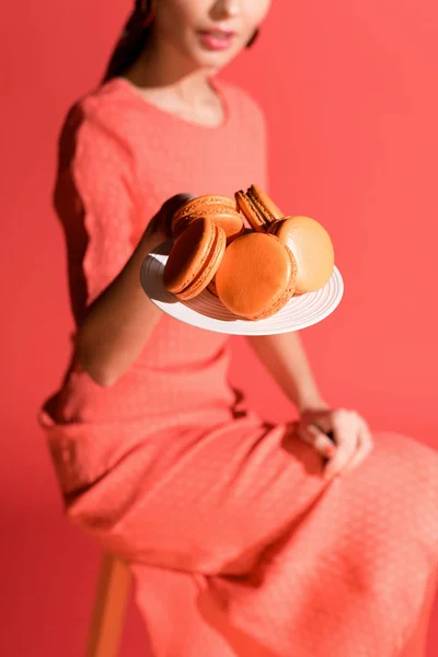 Вибірковий фокус жінки, що тримає тарілку з макарунами, ізольовані на живому коралі. Концепція кольору пантона 2019 року — стокове фото