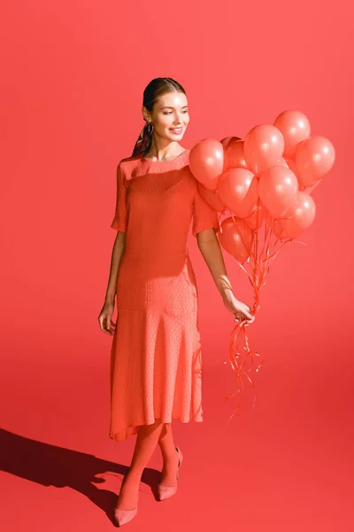 Улыбающаяся модная девушка позирует с живыми коралловыми шариками. Цвет пантона в концепции 2019 года — стоковое фото
