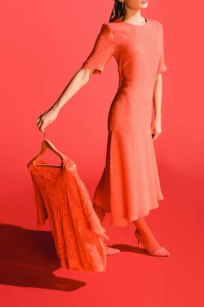 Vista recortada de modelo elegante que sostiene percha con ropa en coral vivo. Pantone color del año 2019 concepto - foto de stock