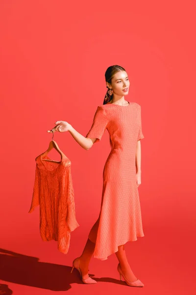 Atractiva mujer elegante sosteniendo percha con ropa en coral vivo. Pantone color del año 2019 concepto - foto de stock