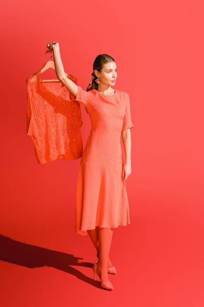 Модна жінка тримає вішалку з одягом на живому коралі. Концепція кольору пантона 2019 року — стокове фото