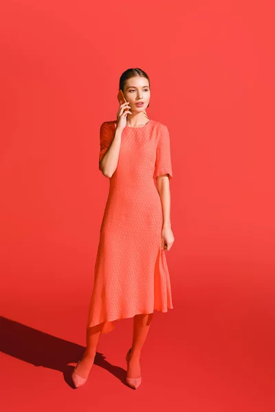 Fashionable woman in living coral dress talking on smartphone on red. Pantone color of the year 2019 concept — Stock Photo