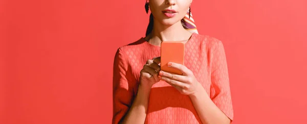 Vue recadrée de fille en robe de corail vivant en utilisant smartphone sur rouge. Couleur Pantone de l'année 2019 concept — Photo de stock