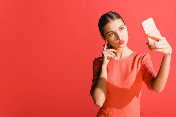 Attractive woman in living coral dress taking selfie on smartphone on red. Pantone color of the year 2019 concept — Stock Photo