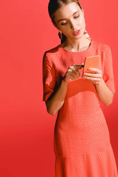 Mulher atraente em viver vestido de coral usando smartphone no vermelho. Pantone cor do ano 2019 conceito — Fotografia de Stock