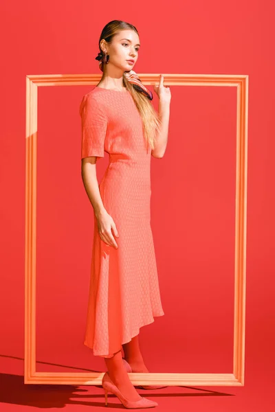 Fashionable young woman in trendy dress posing with big frame on living coral. Pantone color of the year 2019 concept — Stock Photo