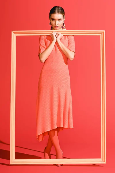 Fille élégante à la mode en robe posant avec un grand cadre sur le corail vivant. Couleur Pantone de l'année 2019 concept — Photo de stock