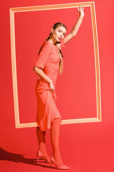 Модная фотосессия со стильной моделью в платье, позирующей с большой рамкой на живом коралле. Цвет пантона в концепции 2019 года — стоковое фото