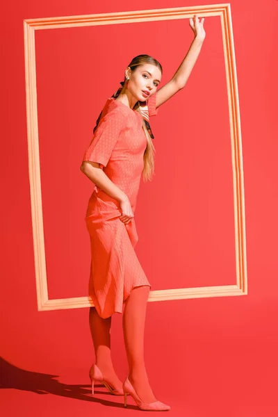 Pousse de mode avec modèle élégant en robe posant avec grand cadre sur corail vivant. Couleur Pantone de l'année 2019 concept — Photo de stock