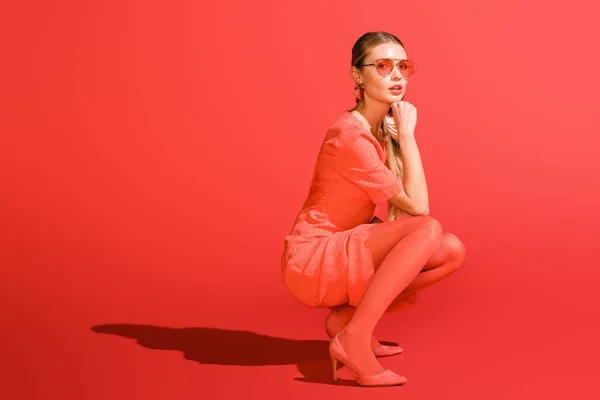 Modelo elegante posando en ropa de coral vivo y gafas de sol sobre fondo rojo - foto de stock